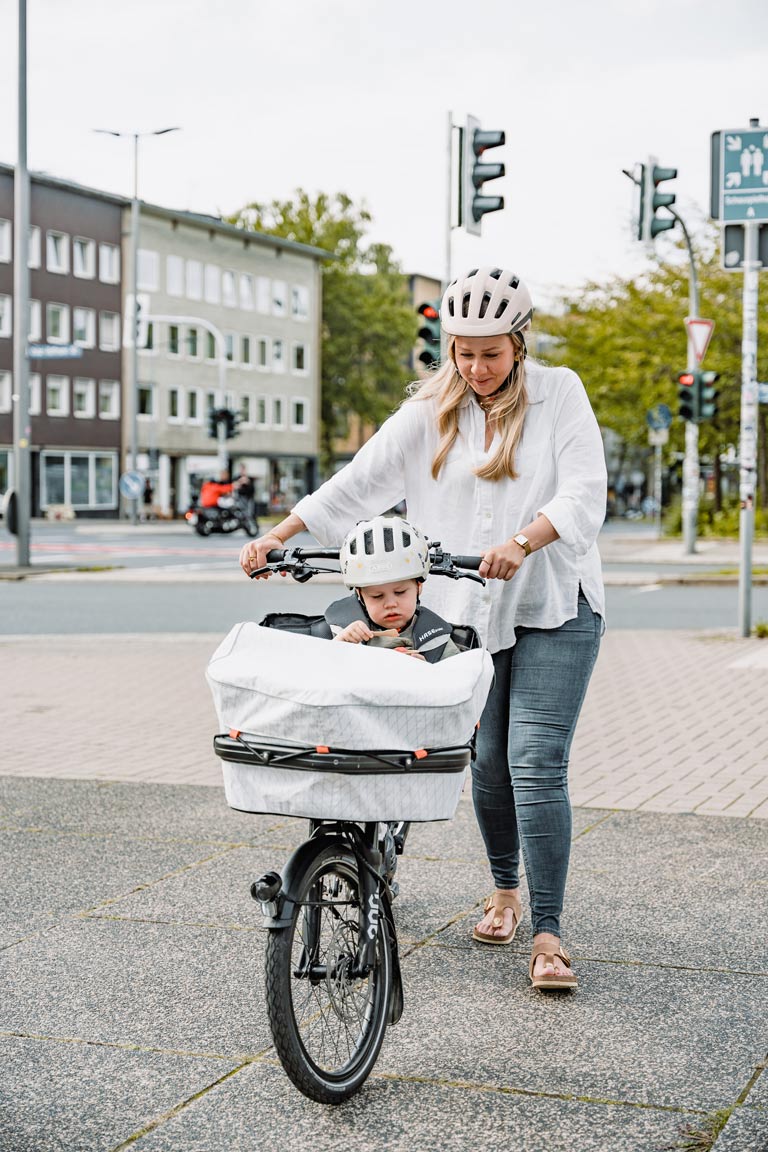 Eine junge Mutter schiebt das Hase Bikes Gravit City E mit ihrem Kind in der Textilbox